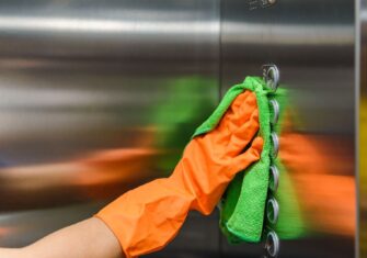 Person cleaning elevator buttons with a green rag. What Are Sustainable Janitorial Services and What Do They Look Like in Practice?